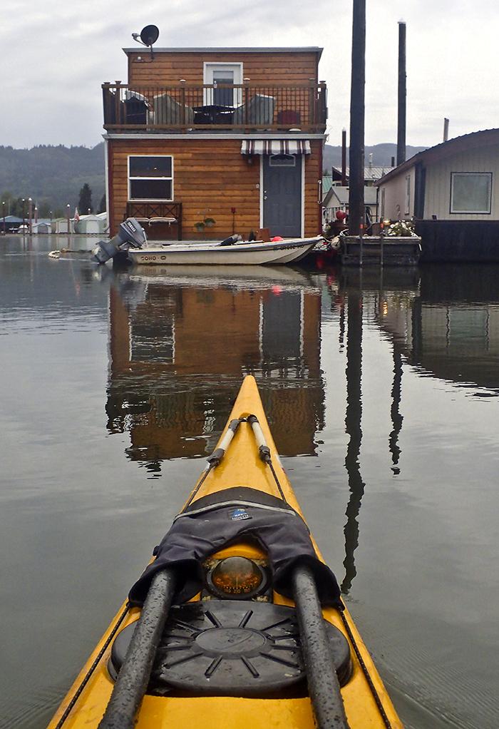 kayak bow faces toward a floating home with a small power boat parked in front