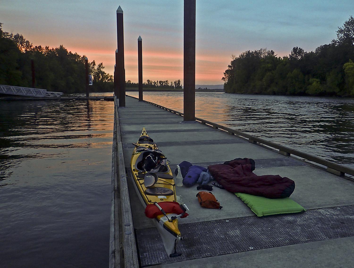 camping on a dock at sunset, sleeping bag and other affects laid out by kayak
