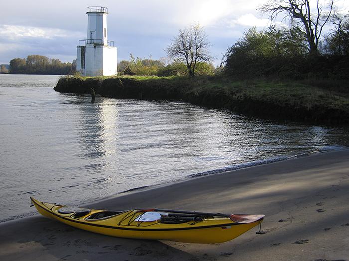 kayak ashore, warrior rock lighthouse juts out on a peninsula in the background