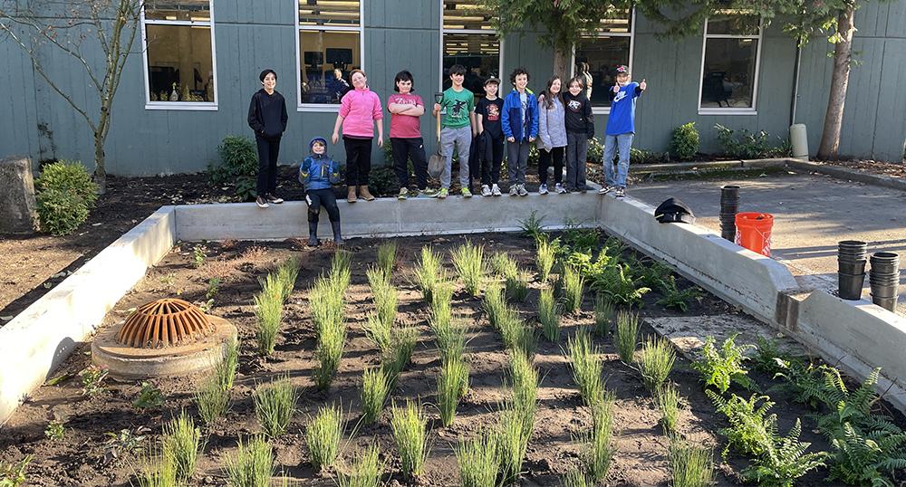 10 students stand behind a newly planted bioswale, giving thumbs up