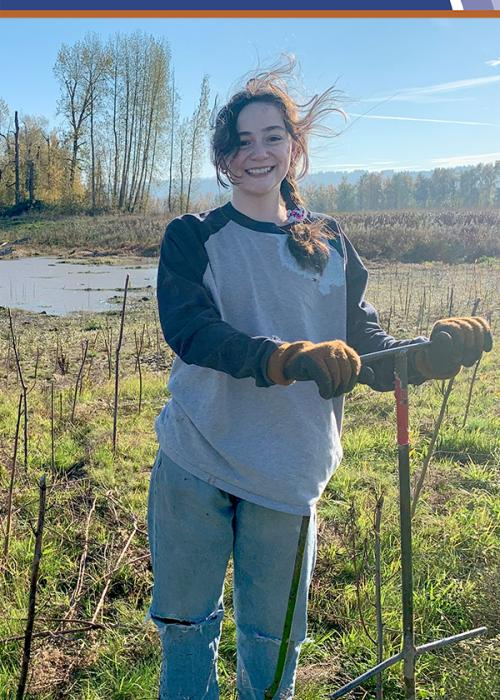 Girl stands and smiles, holding a planting bar